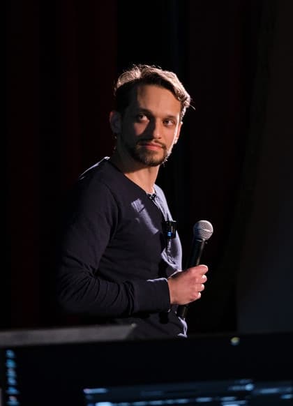A speaker pausing during a talk, lit against a dark stage