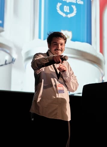 A speaker mid-presentation in front of a bright screen